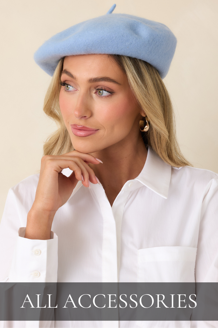 Model wearing a soft blue beret, white blouse, and gold hoop earrings featured in the women’s accessories collection at Red Dress.