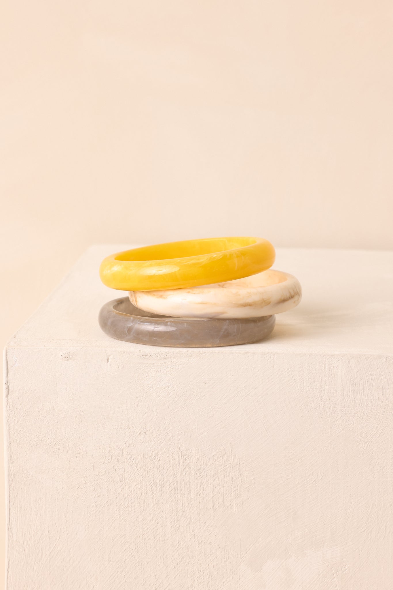 Trio of marbled bangles in yellow, ivory, and grey stacked together.