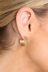 Model shown wearing gold earrings that feature ridged detailing, a twist detailing in the middle of the hoop, and a secure post backing.