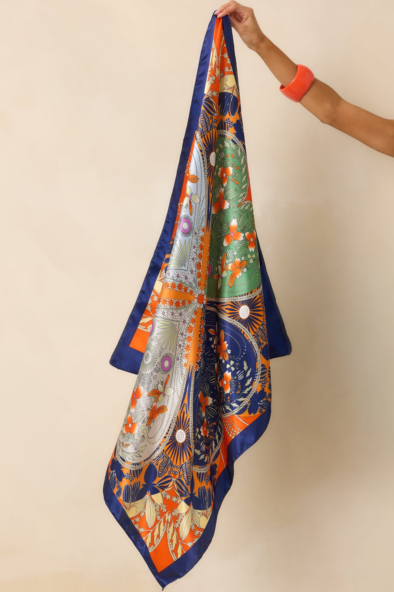 Vibrant orange hair scarf showcasing a patterned geometric design with floral and clover accents and a smooth satin texture. 
