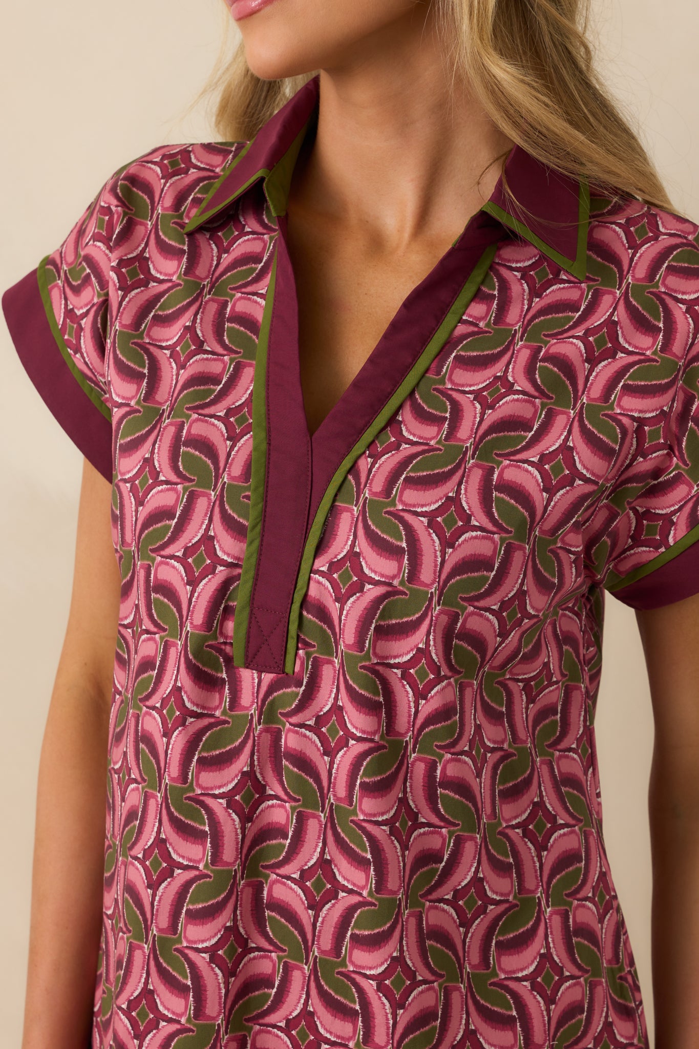 V-neckline with wine purple collar and contrasting green trim against the mauve geometric fabric.