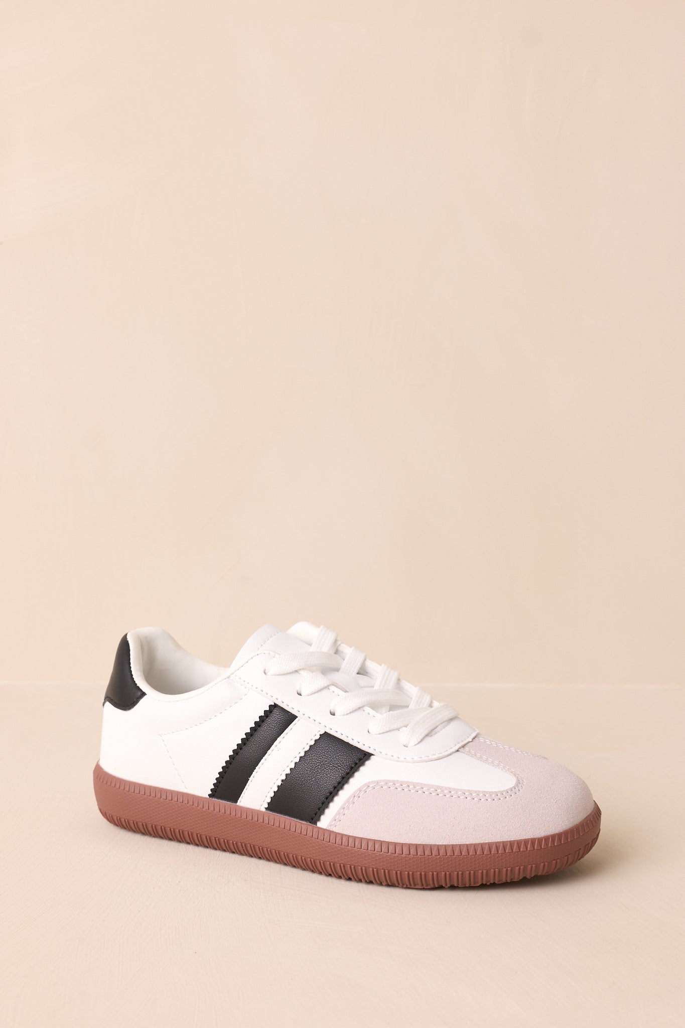 Another front angled view of the white sneakers featuring the round toe, rubber sole, and black faux leather stripes.
