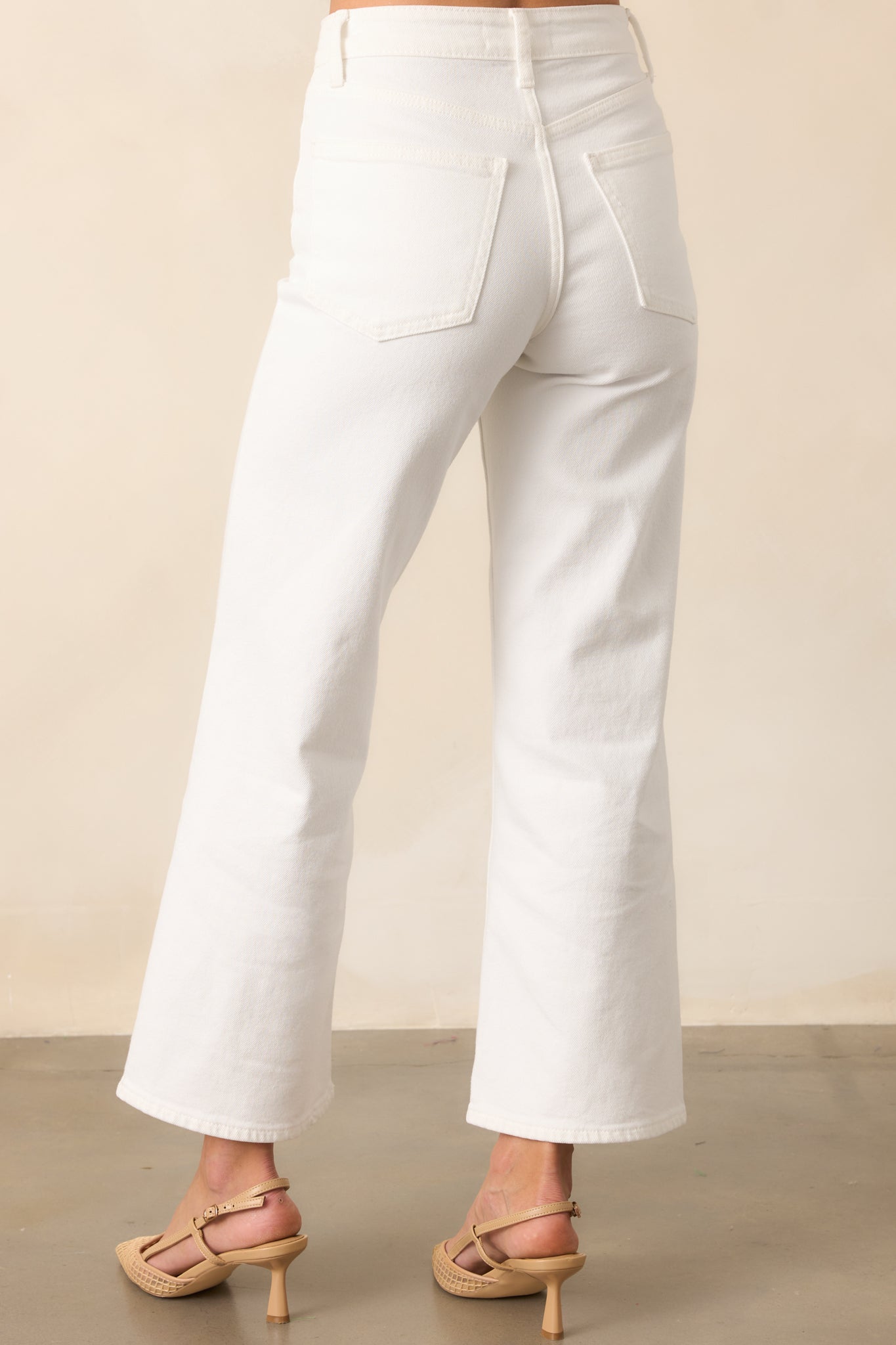 The back view of white high-waisted jeans with functional pockets, belt loops, and a cropped length, highlighting the tailored fit and modern cut.