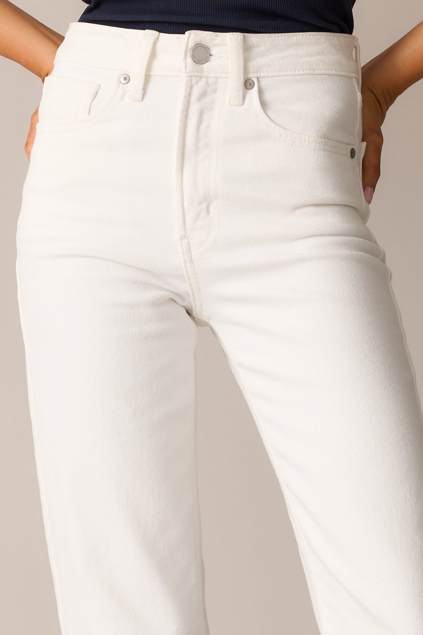 A close-up of the jeans’ button-zipper closure, showcasing the precise stitching and durable white denim.