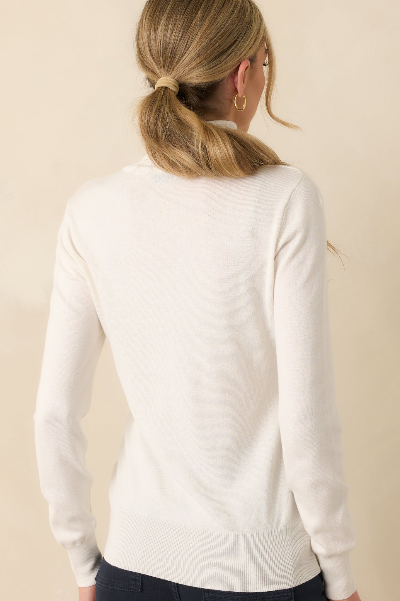 A view from behind of the ivory sweater, showing the continuation of the ribbed hem and cuffs along with the smooth back panel.