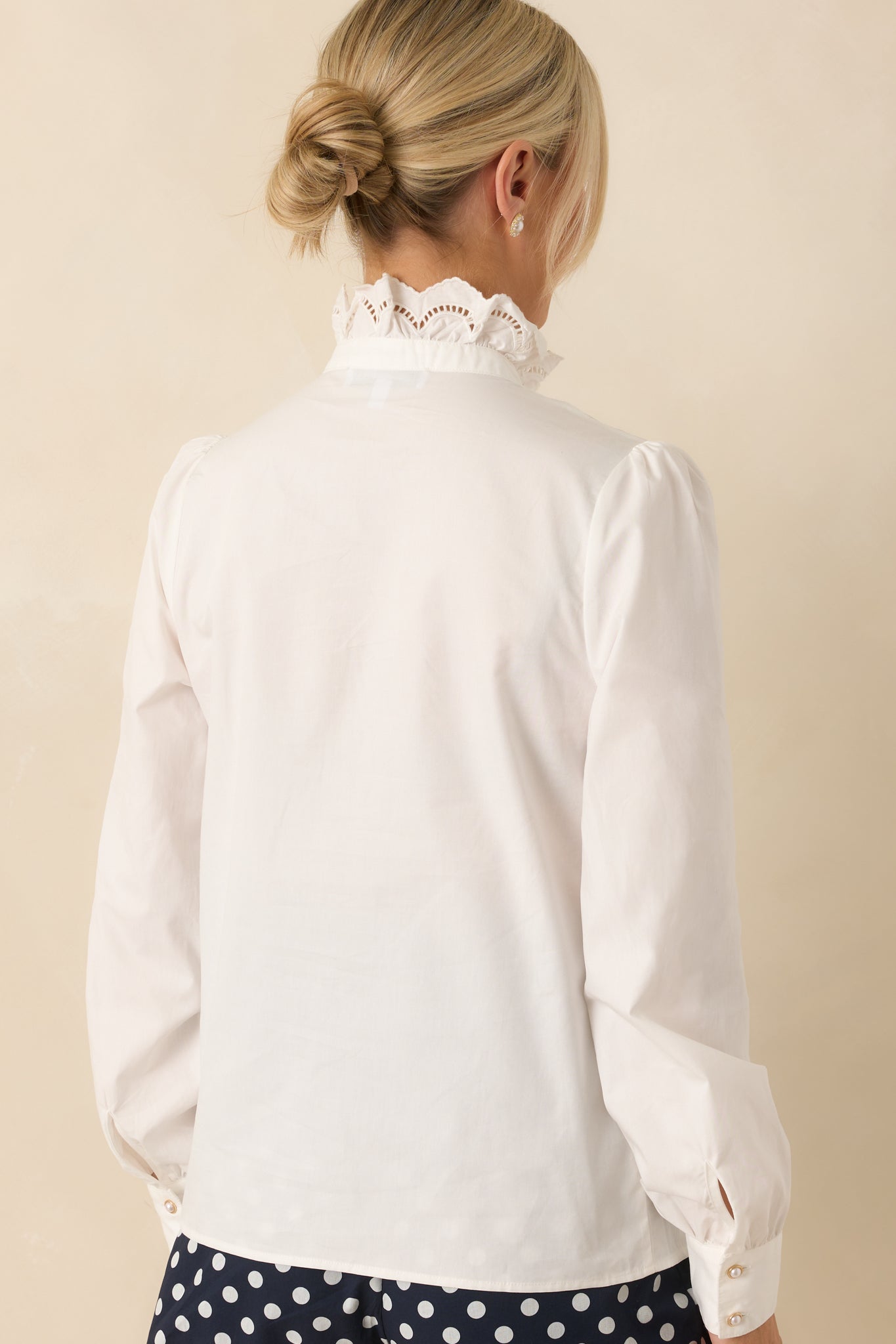 Back view of white long-sleeve blouse showing smooth fabric, puffed sleeves, and ruffled collar silhouette.