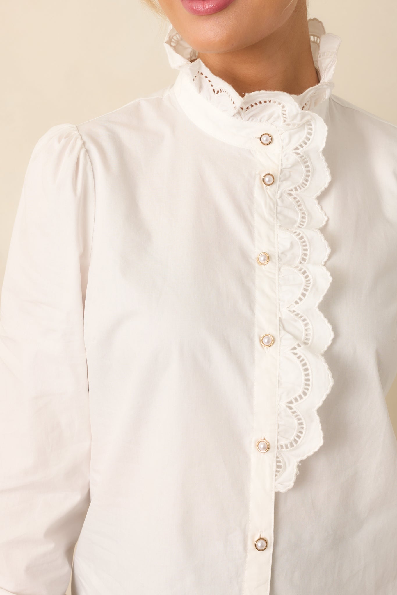 Close-up of white blouse displaying scalloped eyelet lace trim, pearl buttons, and ruffled collar.