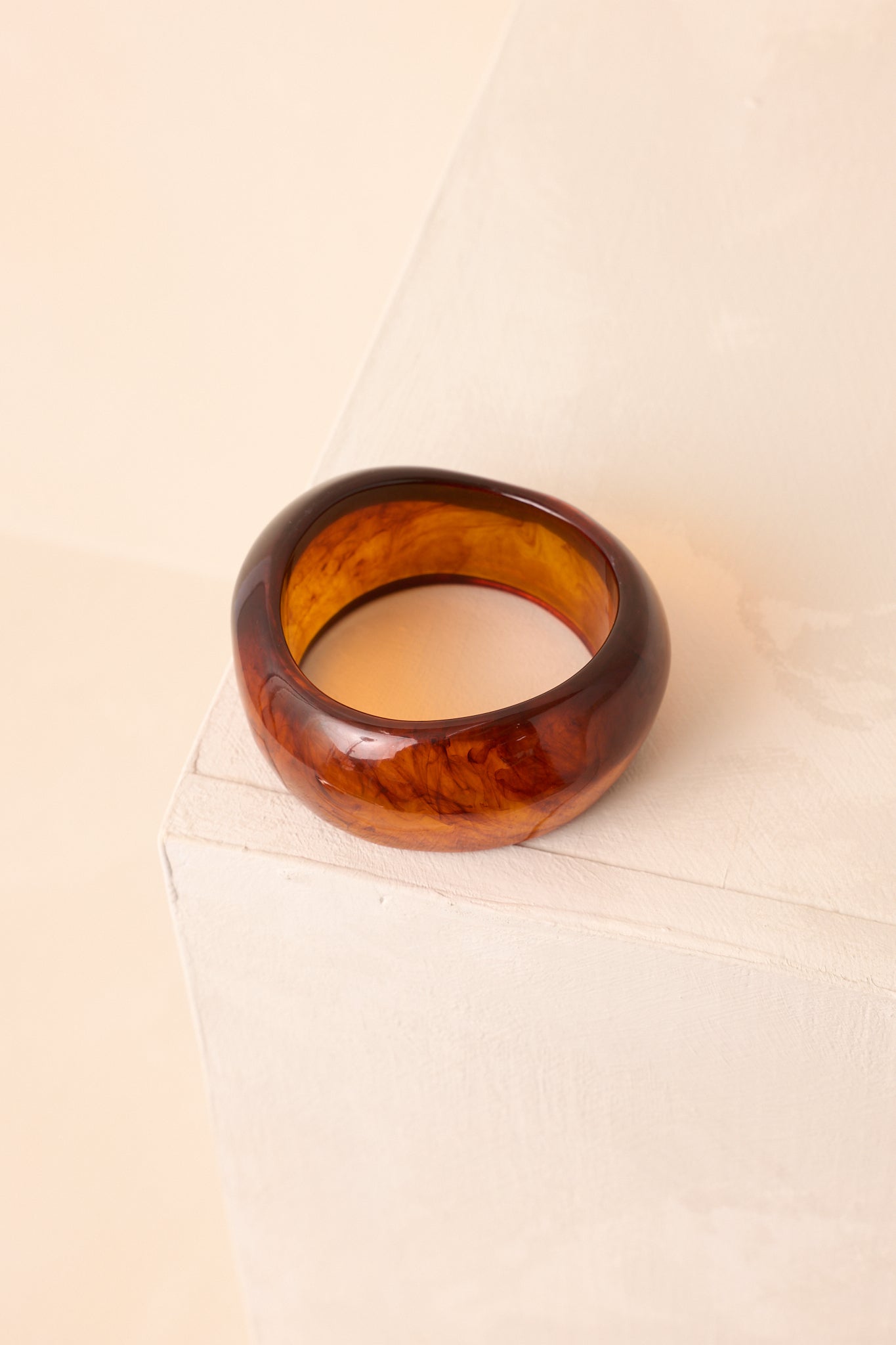 A cropped view of the wide brown tortoise shell bangle emphasizing its smooth surface.
