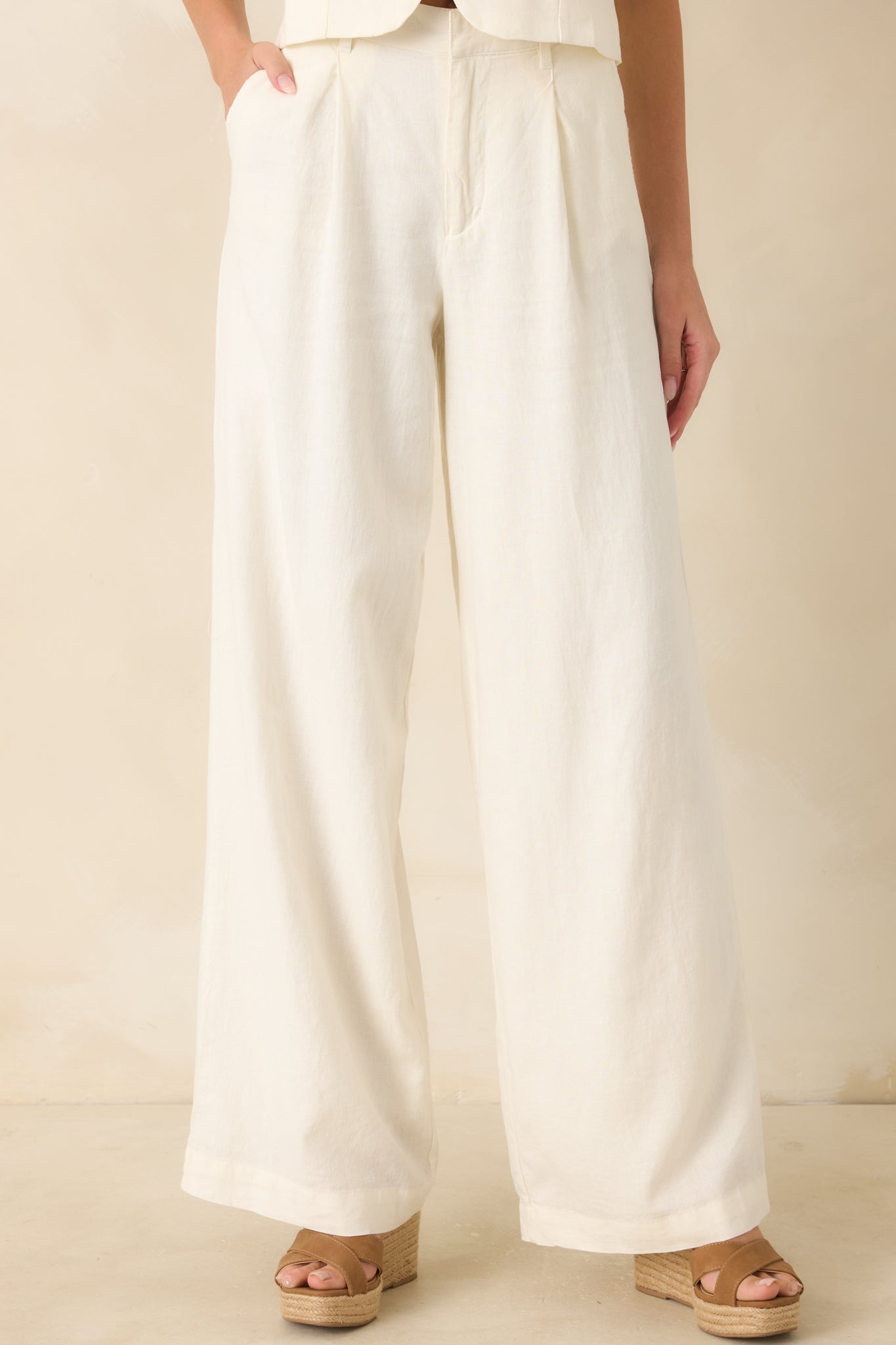 Close view of the ivory pants highlighting the high-rise waistband, zip fly with button closure, and washed linen texture.