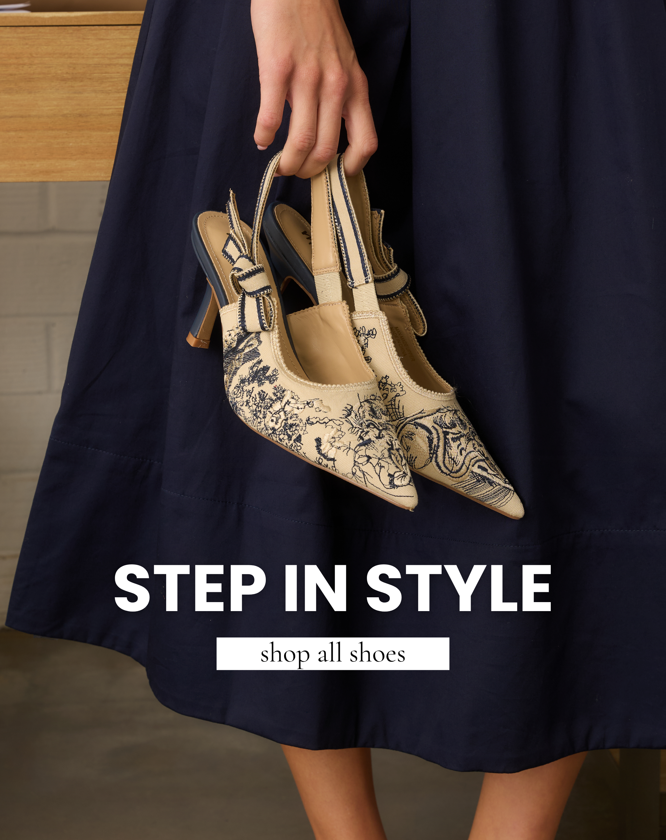 Cream embroidered slingback heels with navy floral detailing and bow accents held by a model. Shoes featured in All Shoes shop.