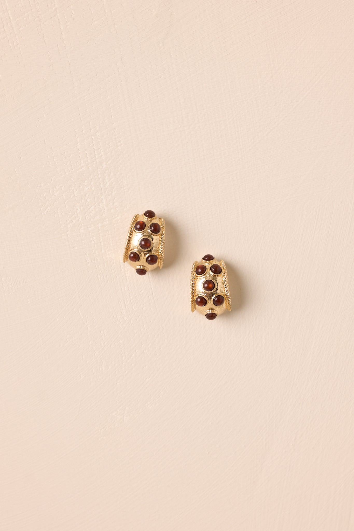 Earrings laid flat against a beige backdrop, emphasizing the bezel set brown stones and open hoop shape.