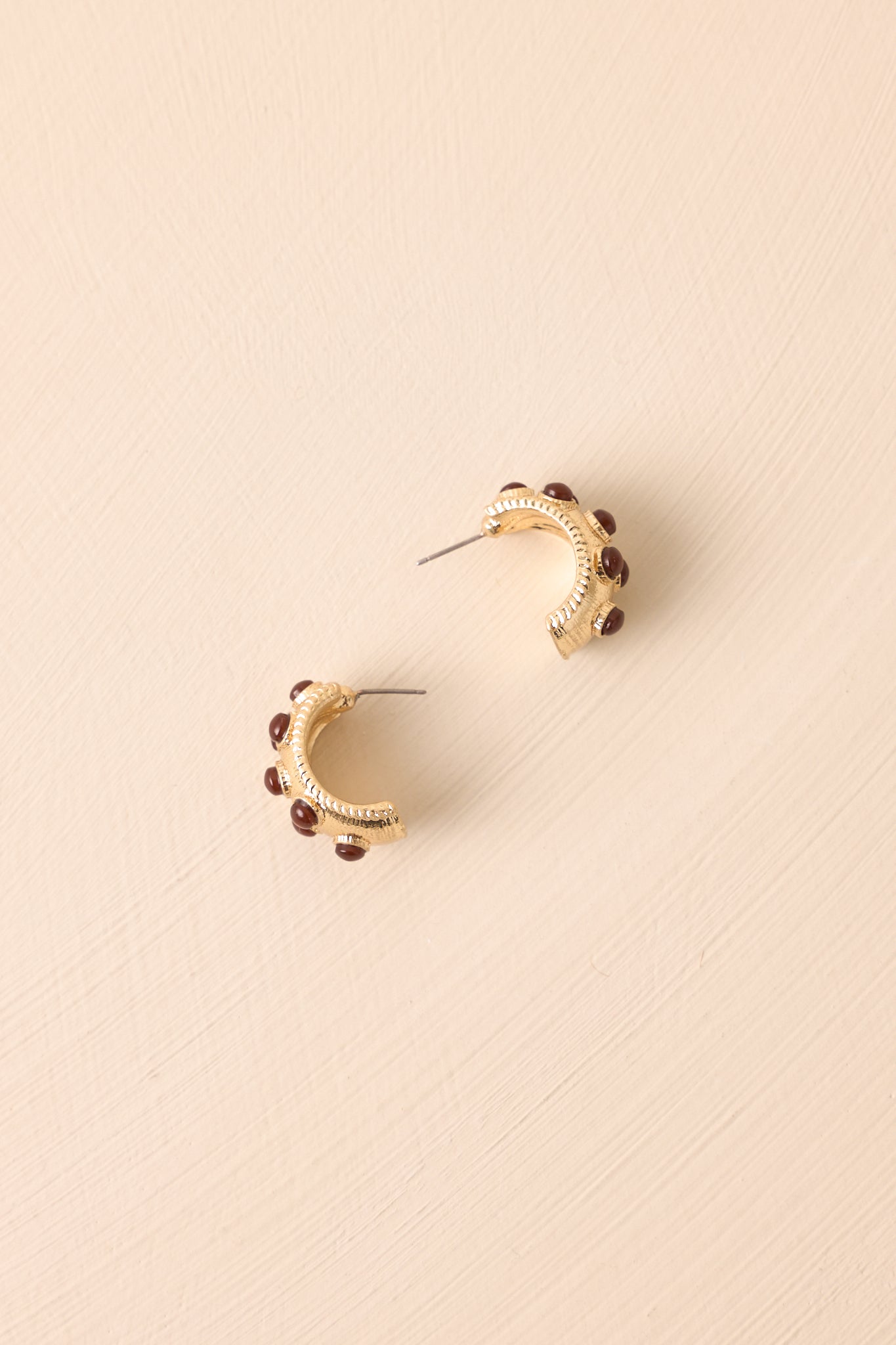 Pair of incomplete hoop earrings displayed on a beige background, showing the worn gold color and textured detailing.