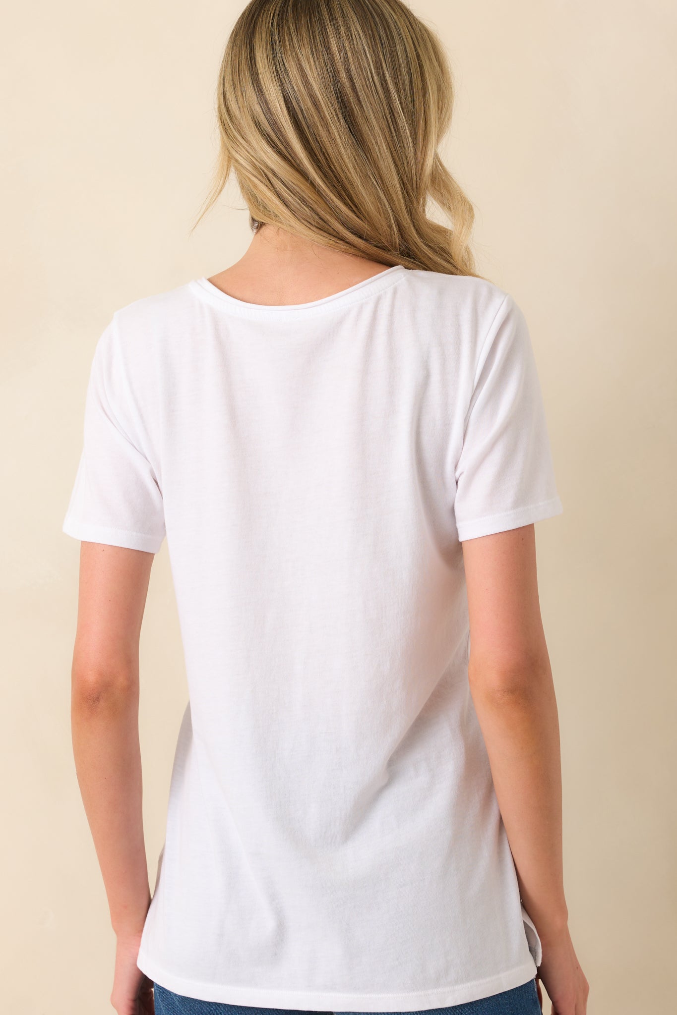 A view from behind of the white tee showing the short sleeves, relaxed shape, and side vent slits at the hem.