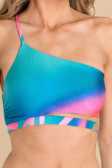 Close up view of this bathing suit top that features a one shoulder neckline with no padding, and adjustable strap, and a colorful additional strap detail under the bustline.