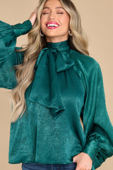 Close up shot of this top that features a high neckline, balloon sleeves with buttons at the cuff, an adjustable self tie around the neck, and a flowy fit. This top can be styled with the self-tie bow in the front or in the back.