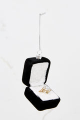 Side view of this engagement ring ornament that features a black box, white sparkly inside, and a gold ring.