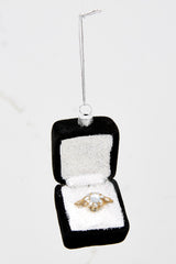 Top view of this engagement ring ornament that features a black box, white sparkly inside, and a gold ring.