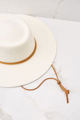 Close up view of this hat that features a round telescope crown with a flat brim and a leather chinstrap around the crown.