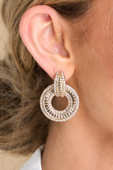 Front view of model wearing earrings featuring dangle hoops, gold hardware with rhinestone encrusting, and post secure backing.