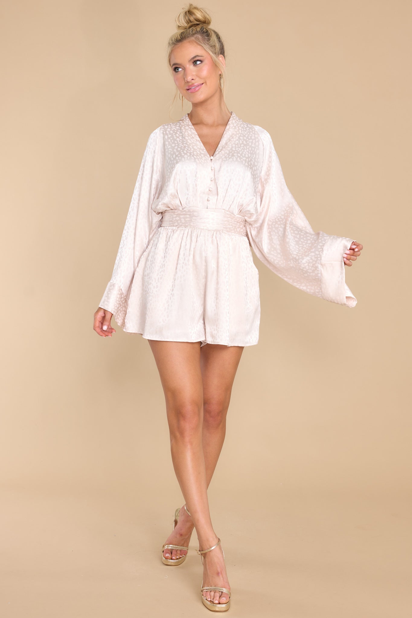 Full body view of this romper that features a v-neckline, buttons down the bust, wide dolman sleeves, functional pockets at the waist, an elastic insert at the back of the waist, and a self tie belt.