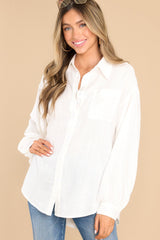 This white top features a collared neckline, functional buttons down the bodice, one pocket on the bust, and wide sleeves with buttoned cuffs. 