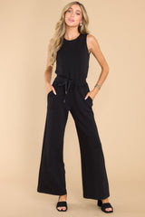 Front view of this jumpsuit that features a round neckline, a keyhole cutout at the back of the neck with a button closure, a stretchy waistband with a self-tie drawstring, functional pockets at the hip, and a wide, flowy leg. 