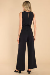 Back view of this jumpsuit that features a round neckline, a keyhole cutout at the back of the neck with a button closure, a stretchy waistband with a self-tie drawstring, functional pockets at the hip, and a wide, flowy leg. 