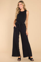 Full body view of this jumpsuit that features a round neckline, a keyhole cutout at the back of the neck with a button closure, a stretchy waistband with a self-tie drawstring, functional pockets at the hip, and a wide, flowy leg. 