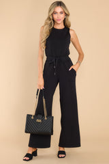 Front view of this jumpsuit that features a round neckline, a keyhole cutout at the back of the neck with a button closure, a stretchy waistband with a self-tie drawstring, and functional pockets at the hip.