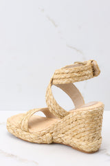 Inner-side view of these shoes that feature an adjustable raffia-style ankle strap with a gold hardware closure, another raffia-style strap over the foot, light padding for added comfort, and an espadrille wedge style heel.