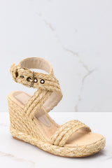 Close up view of these shoes that feature an adjustable raffia-style ankle strap with a gold hardware closure, another raffia-style strap over the foot, light padding for added comfort, and an espadrille wedge style heel.