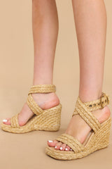 Full view of these shoes that feature an adjustable raffia-style ankle strap with a gold hardware closure, another raffia-style strap over the foot, light padding for added comfort, and an espadrille wedge style heel.