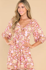This pink dress features a v-neckline with a knot detail in the front and a small cutout below, a smocked insert at the back of the bust, half-length sleeves with elastic cuffs, and a flowy skirt.