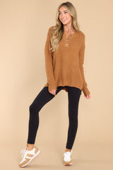 This camel colored sweater features a round neckline with four button closures, long sleeves with tapered cuffs, slits up the sides of the bottom hem, and a waffle knit texture throughout.