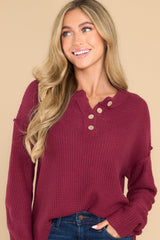 This sangria colored sweater features a round neckline with four button closures, long sleeves with tapered cuffs, slits up the sides of the bottom hem, and a waffle knit texture throughout.