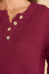 Close up view of this sweater that features a round neckline with four button closures, long sleeves with tapered cuffs, slits up the sides of the bottom hem, and a waffle knit texture throughout.