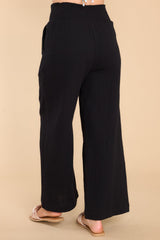 Back view of these pants that features a smock stretch waistband, pockets at the hip, and a wide flowy leg.