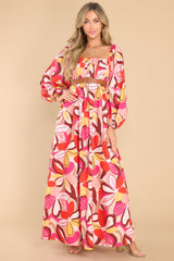 This pink floral dress features a square neckline, pleated detailing along the bust, long puff sleeves with elastic cuffs, a smocked section in the back of the bust, and a vibrant pattern throughout.