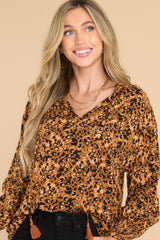 This tan leopard print top features a v-neckline with a self-tie closure, long sleeves with smocked cuffs, and gold metallic detailing throughout.
