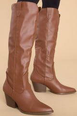 These brown boots feature a pointed toe, a slip-on style, and a stacked heel.