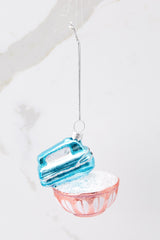 This pink and blue ornament features a design of a blue mixer and a red bowl with faux silver snowflakes.