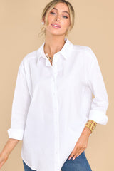 This all white top features a collared neckline, functional buttons down the front, long sleeves with buttoned cuffs, and a scoop bottom hem.