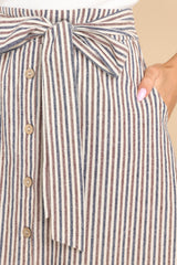 Close up view of this skirt that features a high waist design, a non-removable self-tie belt at the waist, functional buttons down the front, and functional pockets at the hip. 