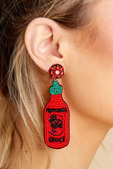 Close up view of these statement earrings that feature a beaded hot sauce bottle design, sewn details, felt back, and a secure lock back fastening.