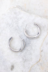 Overhead detailed view of hoop earrings that feature a reflective finish, silver hardware, and a secure post backing.