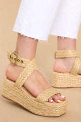 Close up view of these shoes that feature an raffia style strap across the top of the foot, a raffia-style strap that wraps around the ankle with a gold hardware closure, light padding for added comfort, and an espadrille platform design.