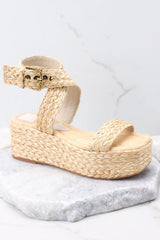 Outer-side view of these shoes that feature an raffia style strap across the top of the foot, a raffia-style strap that wraps around the ankle with a gold hardware closure, light padding for added comfort, and an espadrille platform design.
