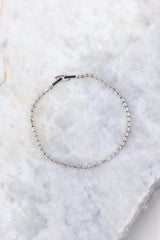 Overhead view of clasped bracelet that features white rhinestones and silver hardware with a fold-over clasp.