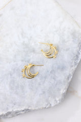 Overhead marble shot of earrings that feature encrusted rhinestones, gold hardware, 3 layered hoops, and a secure post backing. 