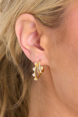 Front shot of model wearing earrings that feature encrusted rhinestones, gold hardware, 3 layered hoops, and a secure post backing. 